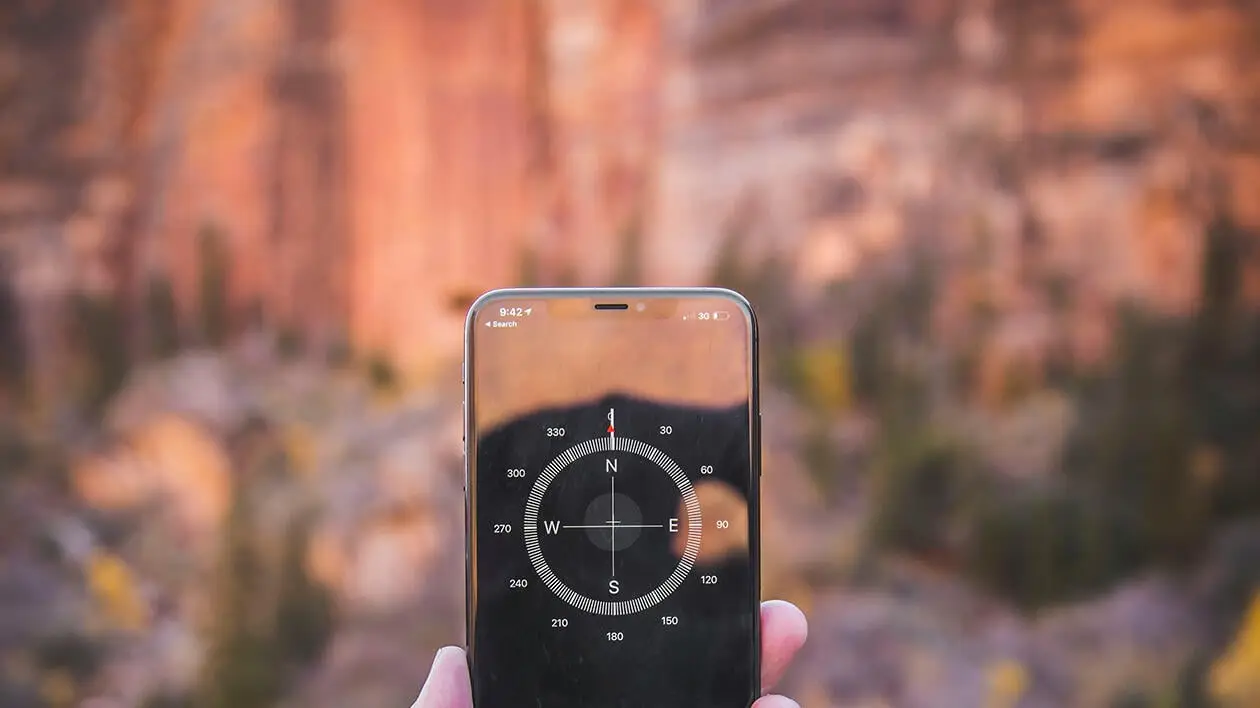 Mann hält Handy mit Kompass-App in der Hand, im Hintergrund ist eine Berglandschaft zu sehen
