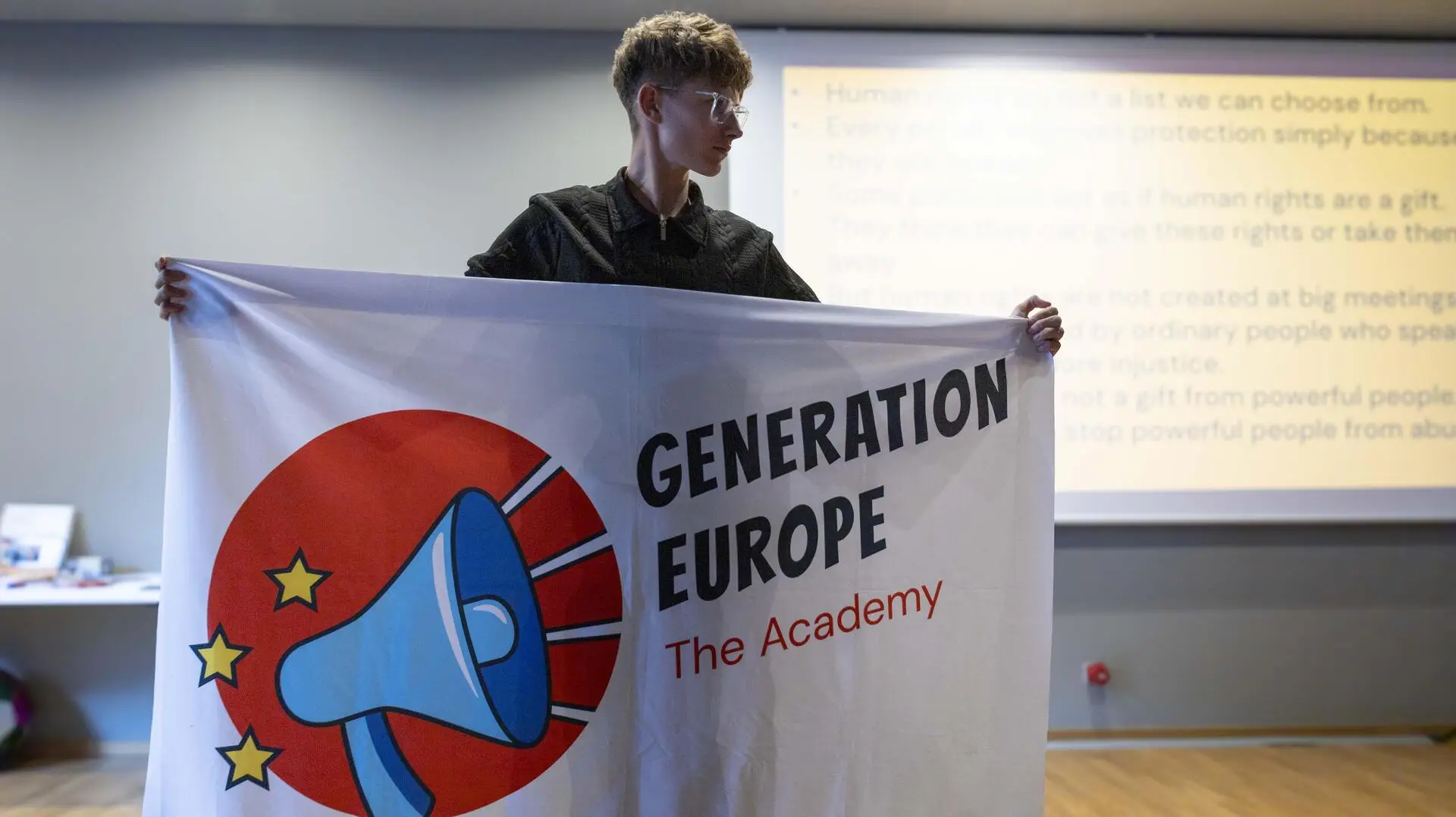 Junger Teilnehmer hält eine Flagge mit der Aufschrift "Generation Europe - The Academy" hoch