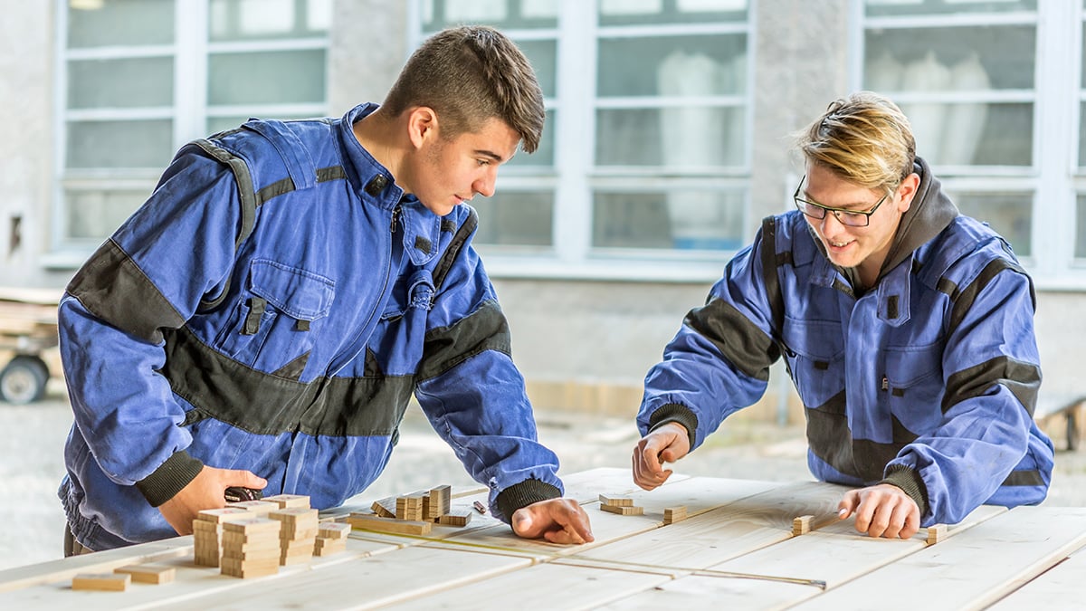 Zwei junge Männer an einem Werktisch in Arbeitskleidung