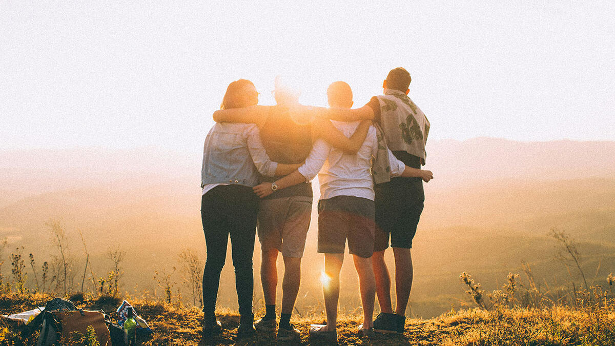 4 Jugendliche stehen während des Sonnenuntergangs auf einem Berg und umarmen sich