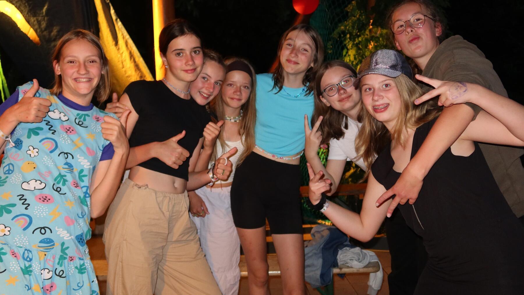 Fröhliche junge Menschen in Sommerkleidung und Daumen hoch bzw. Friedenszeichen im Ferienlager