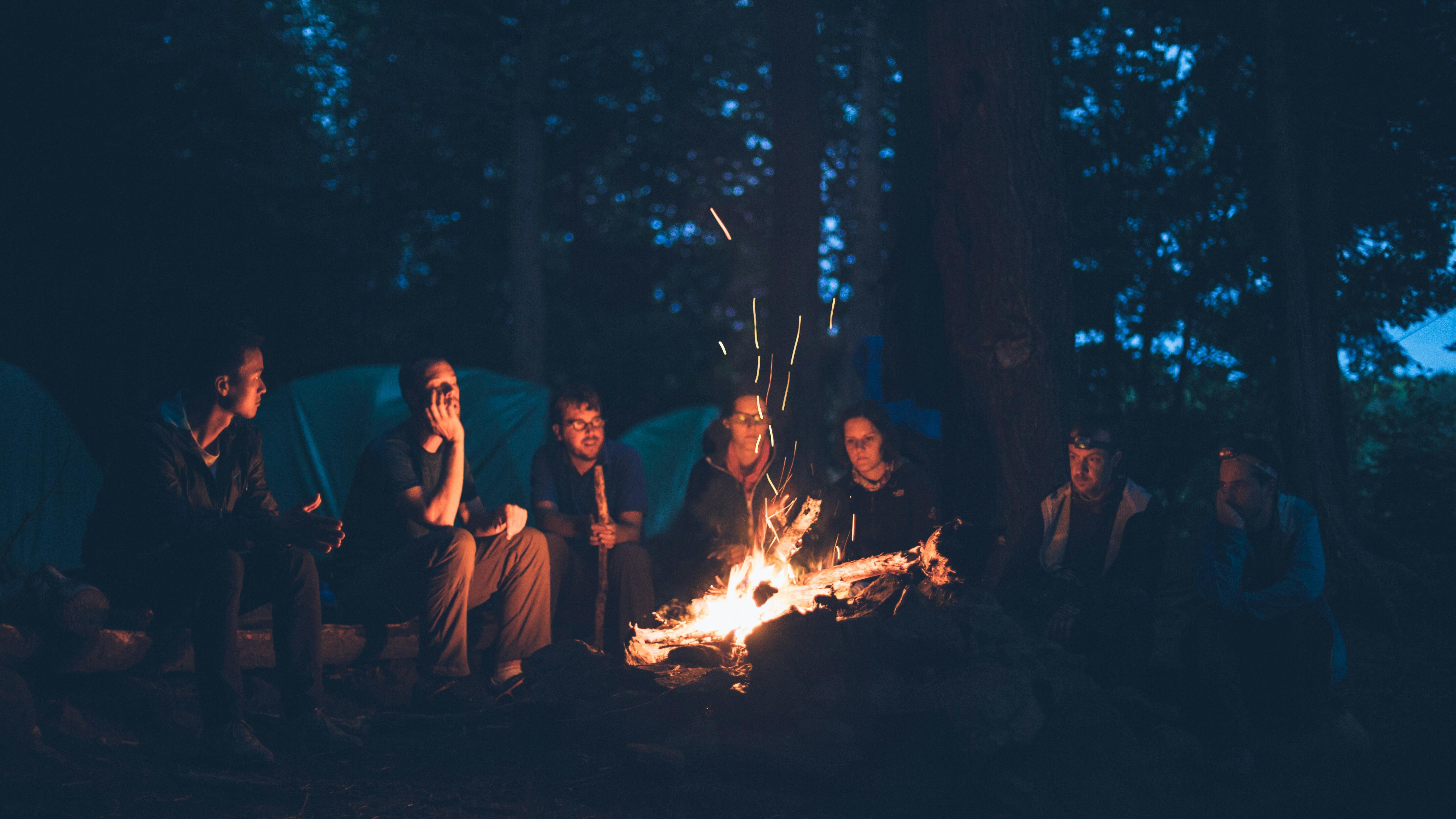 Junge Menschen sitzen im Kreis vor einem Lagerfeuer
